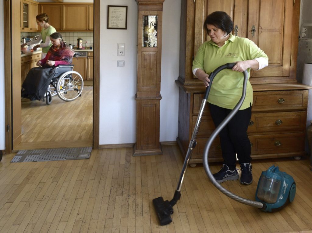 Mitarbeiterin des Pflegeteams am See beim Staubsaugen in der Wohnung einer Kundin